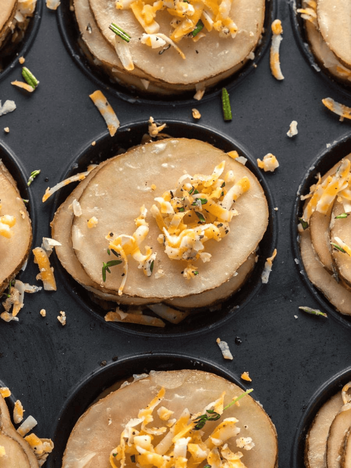 Thin potato slices layered with cheese and herbs in a muffin tin.