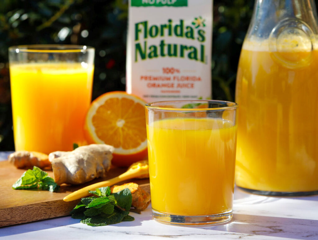 Orange juice set up outdoor with juice in a cup and some ginger and orange in the background