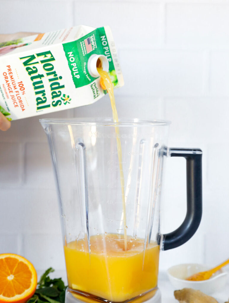 ingredients in the blender with orange juice being poured into the blender