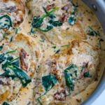 Golden chicken breasts with sun-dried tomatoes and wilted spinach in a creamy skillet sauce.