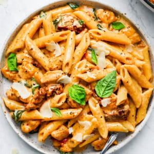 A plate of creamy sun-dried tomato pasta with fresh basil and parmesan shavings on top.