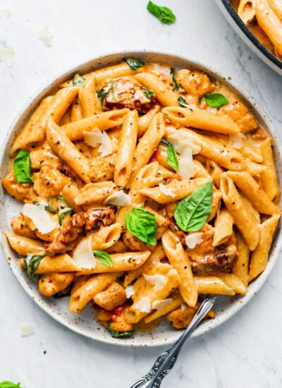 A plate of creamy sun-dried tomato pasta with fresh basil and parmesan shavings on top.