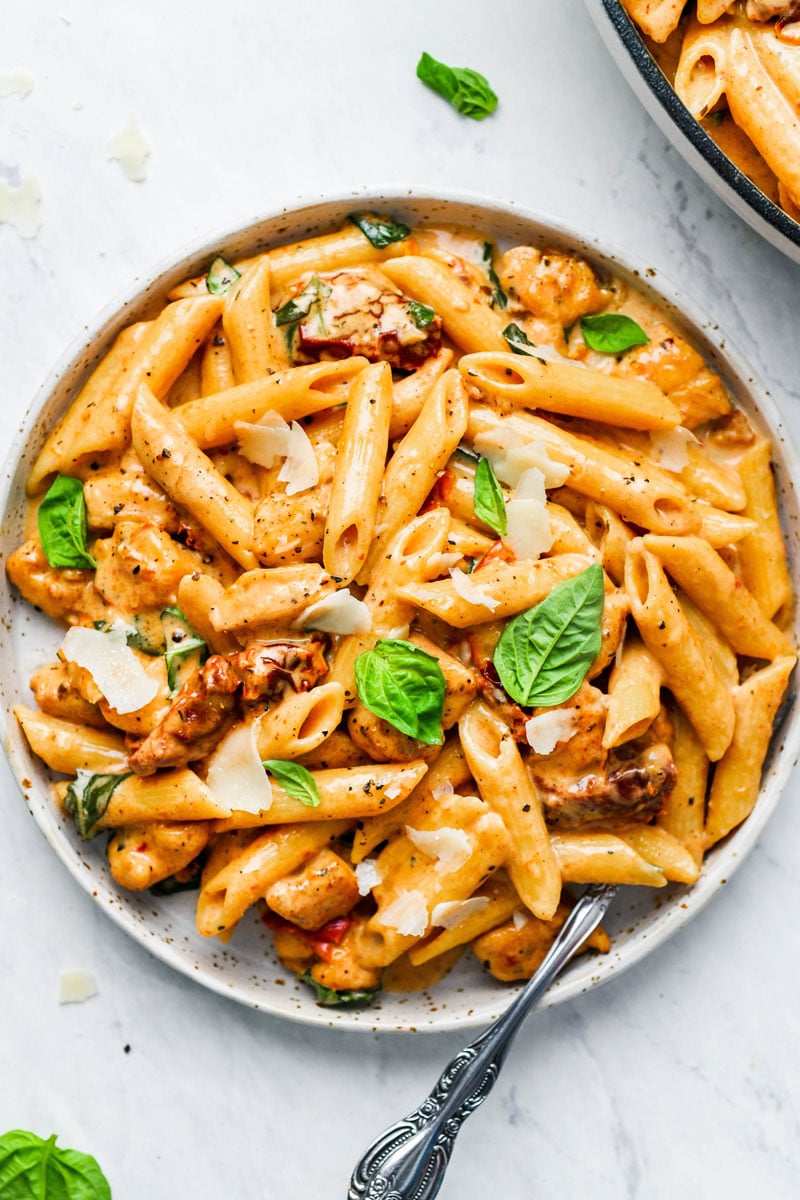 A plate of creamy sun-dried tomato pasta with fresh basil and parmesan shavings on top.