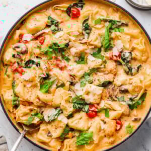 creamy-chicken-tortellini-pasta in a skillet, garnished with basil and shaved parmesan cheese