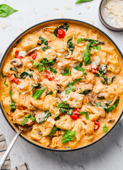 creamy-chicken-tortellini-pasta in a skillet, garnished with basil and shaved parmesan cheese