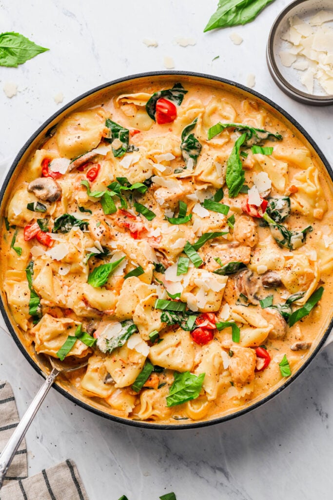 creamy-chicken-tortellini-pasta in a skillet, garnished with basil and shaved parmesan cheese