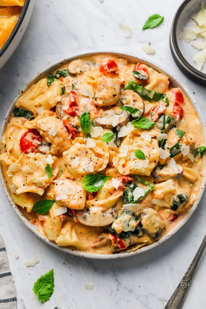 creamy chicken mushroom tortellini pasta served on a plate and garnished with basil and cheese