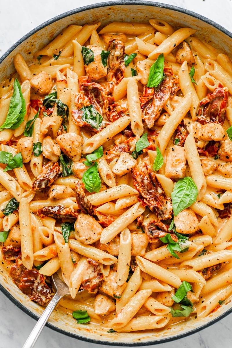 Close up of sun-dried pasta in a pot with fresh basil on top.