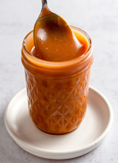 Close up of caramel sauce in a jar with a spoon.