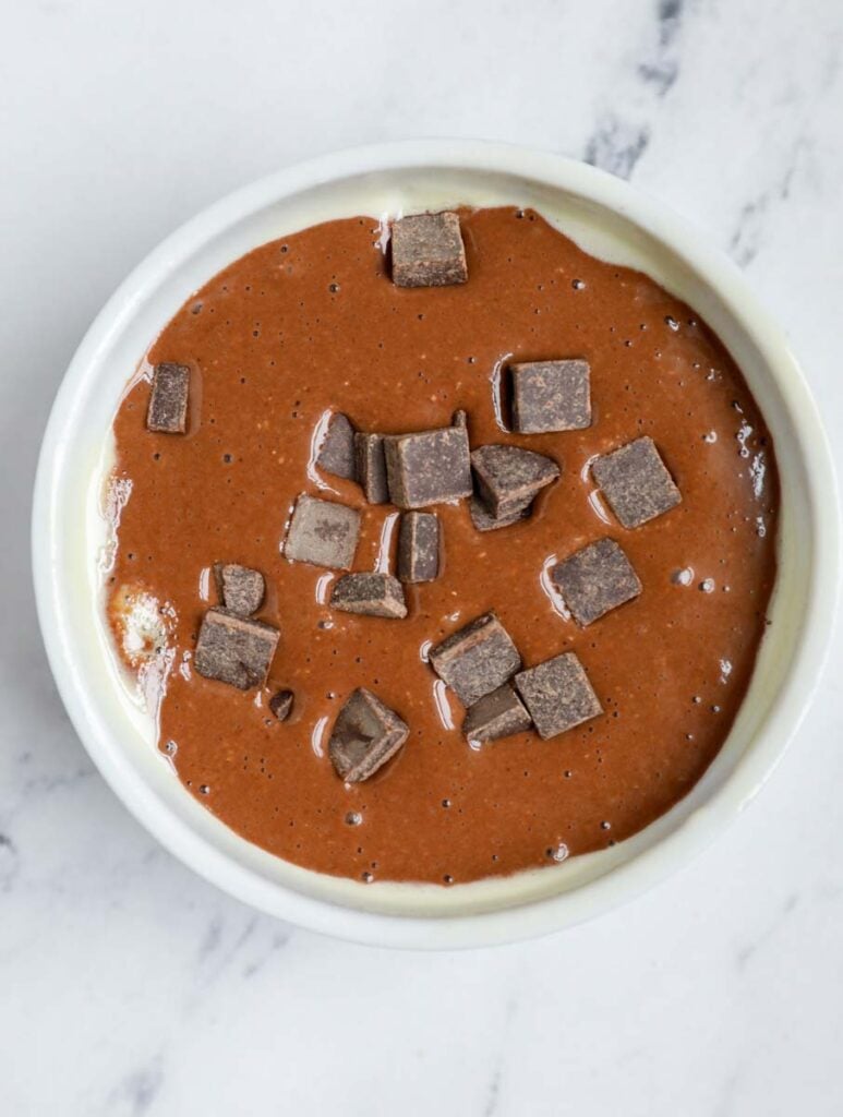 Chocolate peanut butter baked oats batter in a ramekin with chocolate chunks on top.