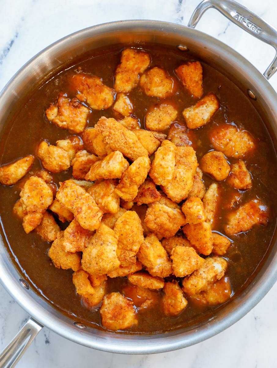 Adding crispy orange chicken into the sauce in a pan.