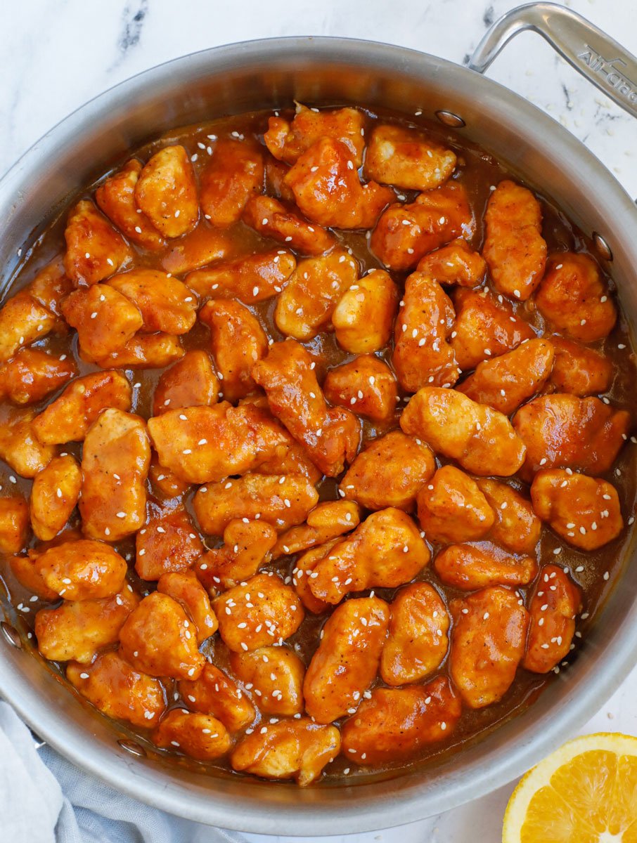Healthy baked orange chicken in a pan covered in sauce.