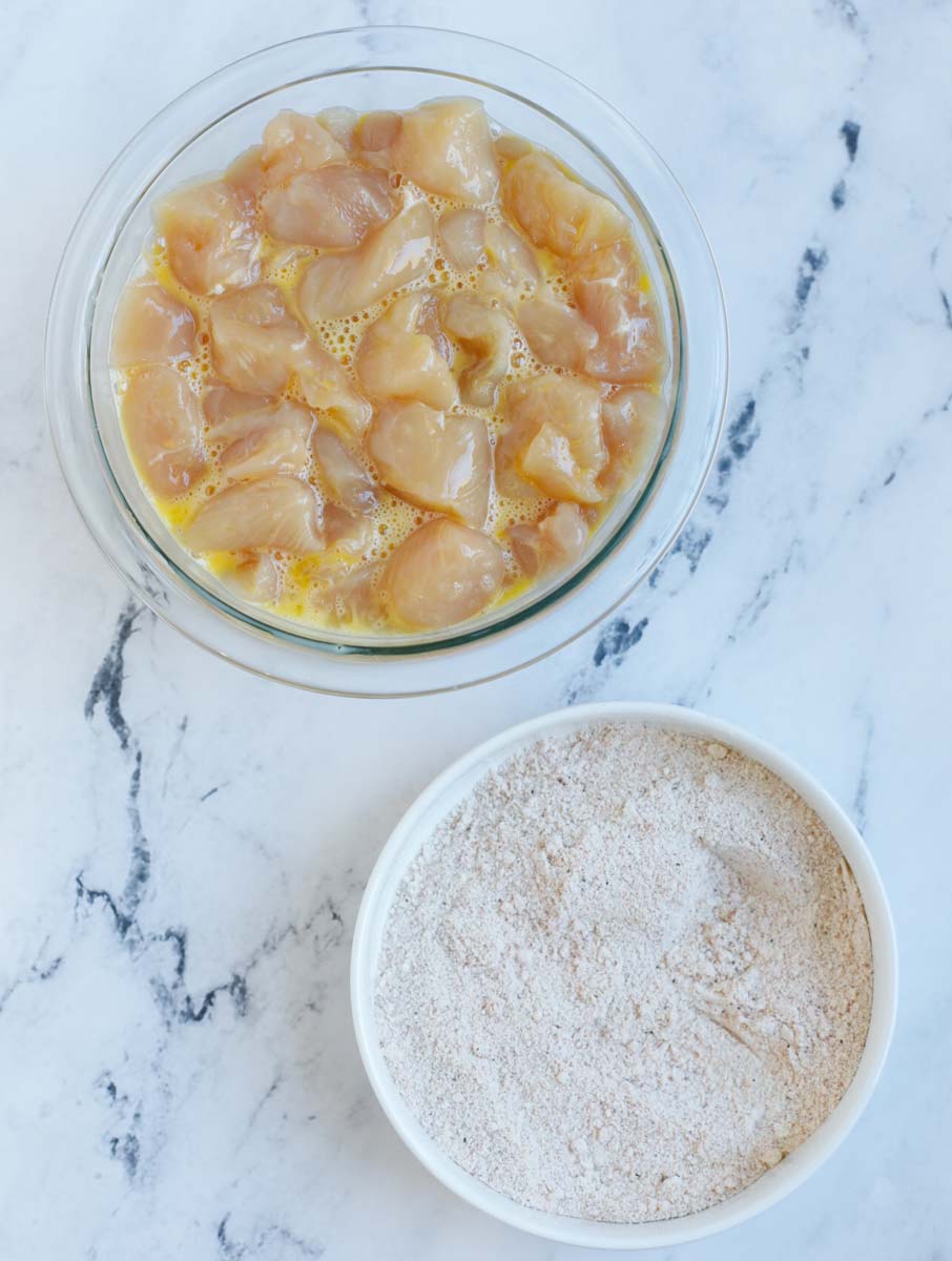 Chicken cubes in egg mixture beside a bowl of breading.