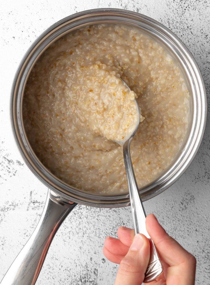 cooked oatmeal in a pot with a spoon scooping some oatmeal