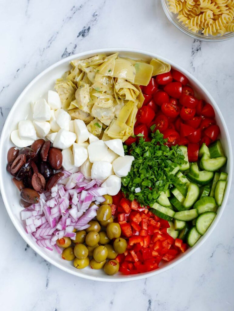 A bowl with all the vegetables for a pasta salad in a bowl.