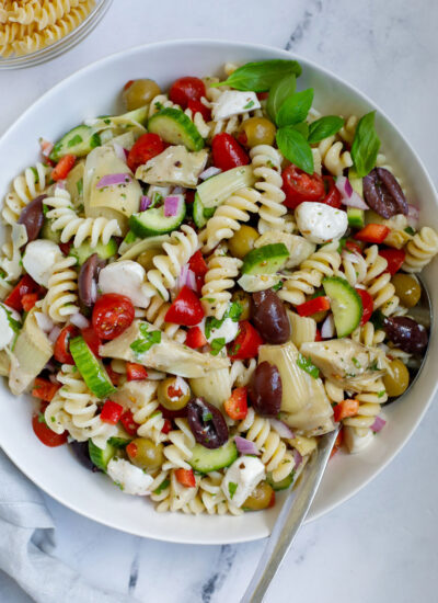 A bowl of Mediterranean pasta salad with a spoon on a marble service.