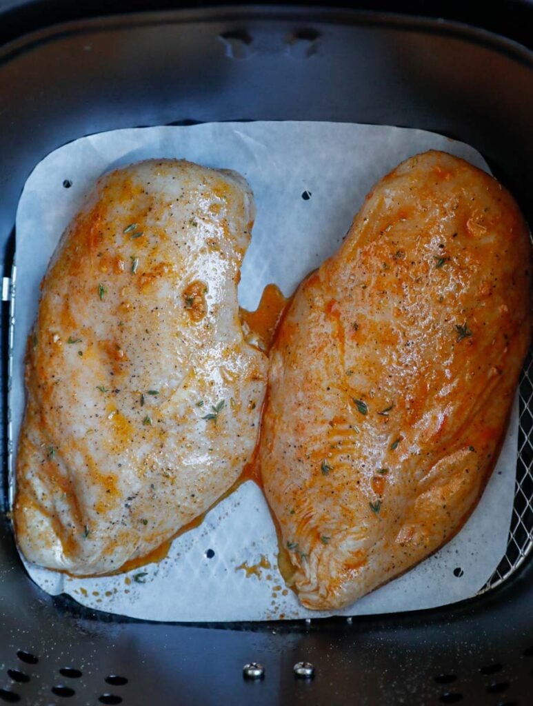 Two chicken breasts in an air fryer basket.