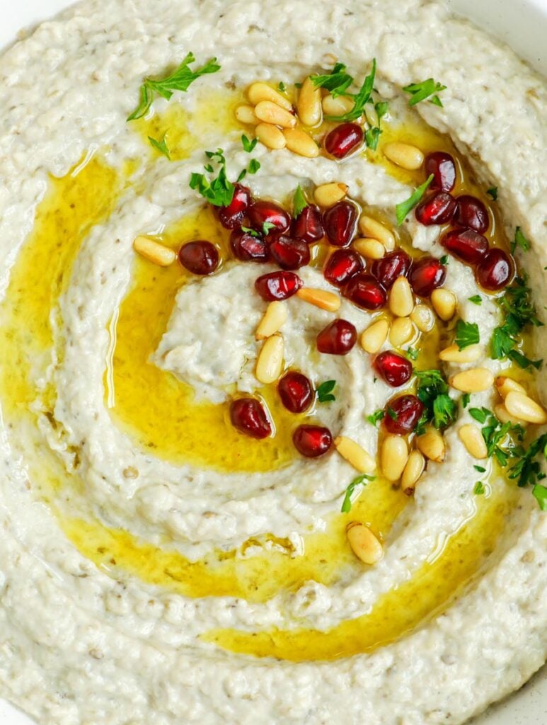 baba ghanouj in a plate topped with olive oil, toasted pine nuts and pomegranate seeds