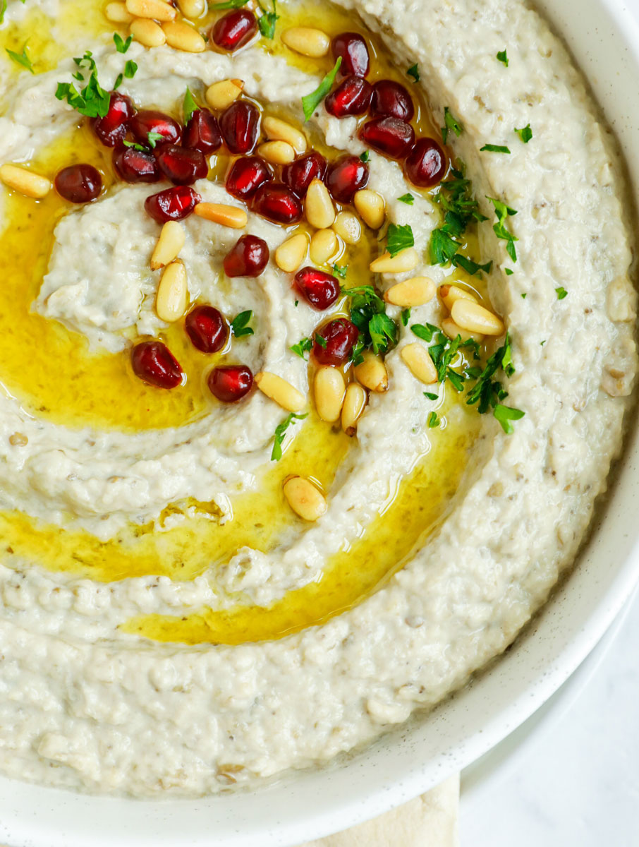 baba ghanouj in a plate topped with olive oil, toasted pine nuts and pomegranate seeds