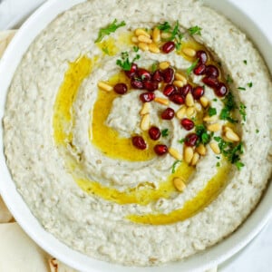 baba ghanouj in a plate topped with olive oil, toasted pine nuts and pomegranate seeds