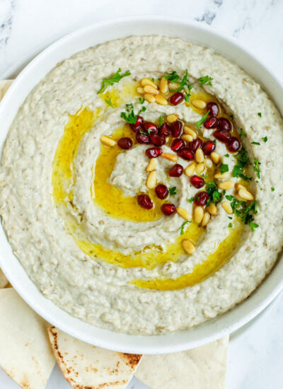 baba ghanouj in a plate topped with olive oil, toasted pine nuts and pomegranate seeds