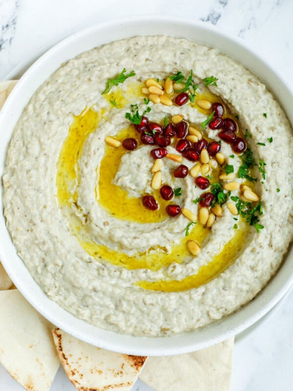 baba ghanouj in a plate topped with olive oil, toasted pine nuts and pomegranate seeds