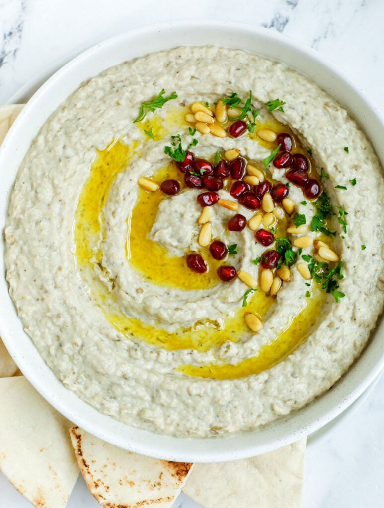 baba ghanouj in a plate topped with olive oil, toasted pine nuts and pomegranate seeds