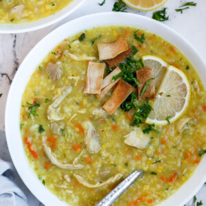 A bowl of chicken lentil soup with fried pita and lemon as garnish.