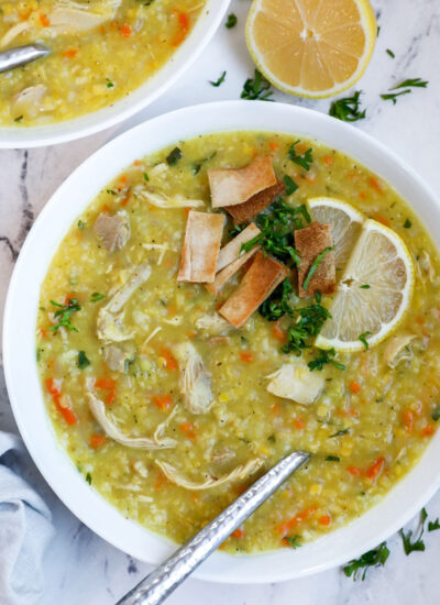 A bowl of chicken lentil soup with fried pita and lemon as garnish.