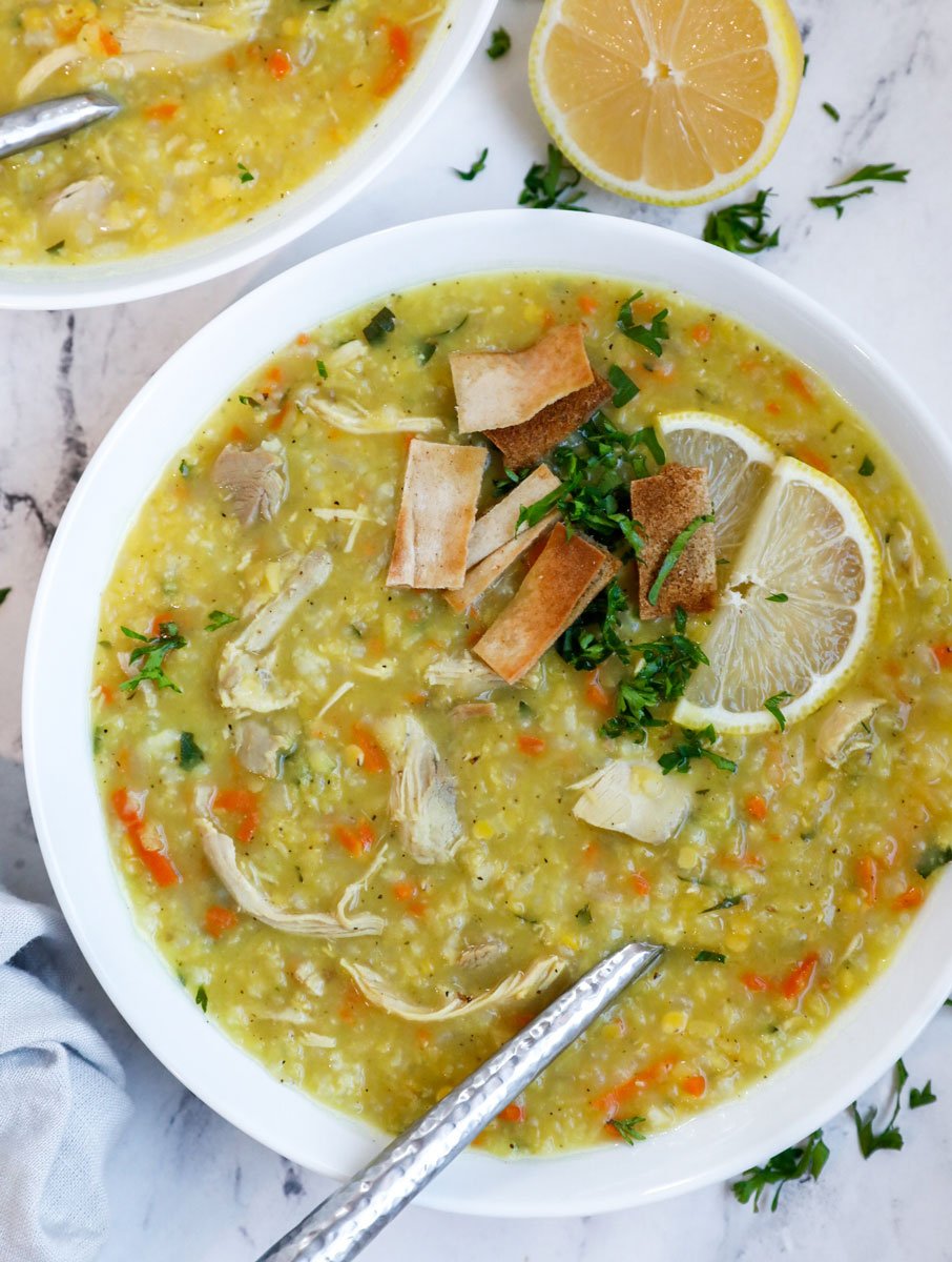 A bowl of chicken lentil soup with fried pita and lemon as garnish.