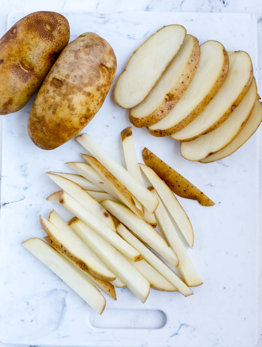 Potatoes cut to the shape of french fries on a cutting board.