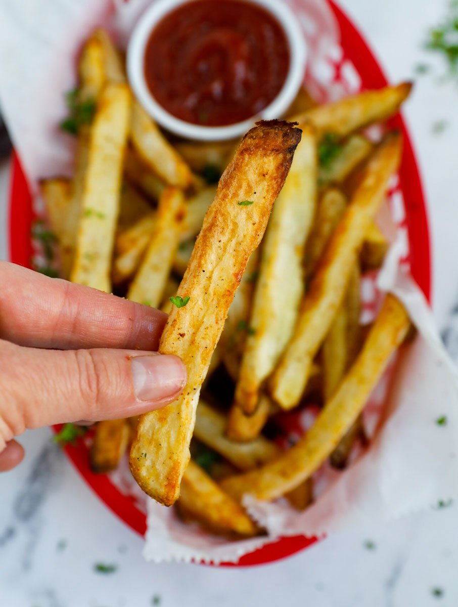 A hand holding up a crispy air fryer french fry.