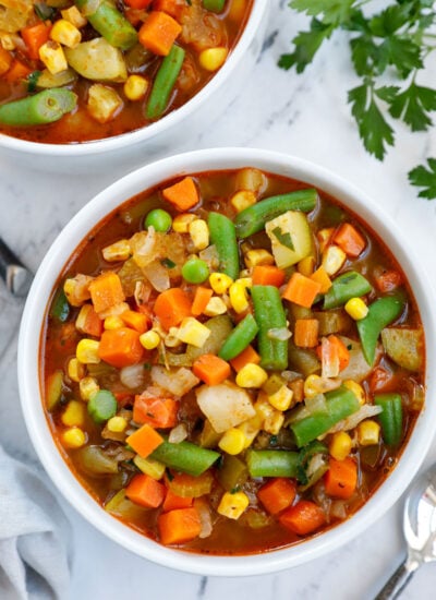 A white bowl of soup packed with veggies as a homemade vegetable soup.