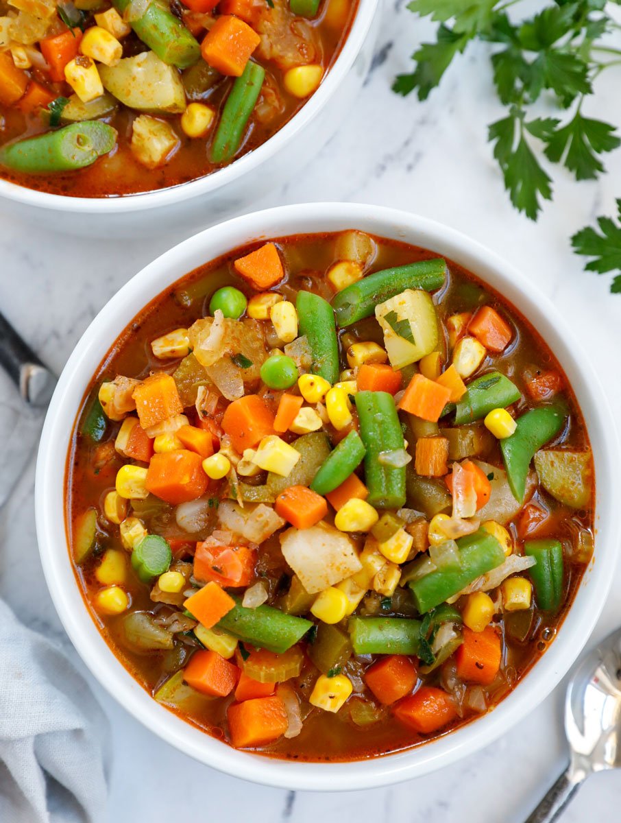 A white bowl of soup packed with veggies as a homemade vegetable soup.