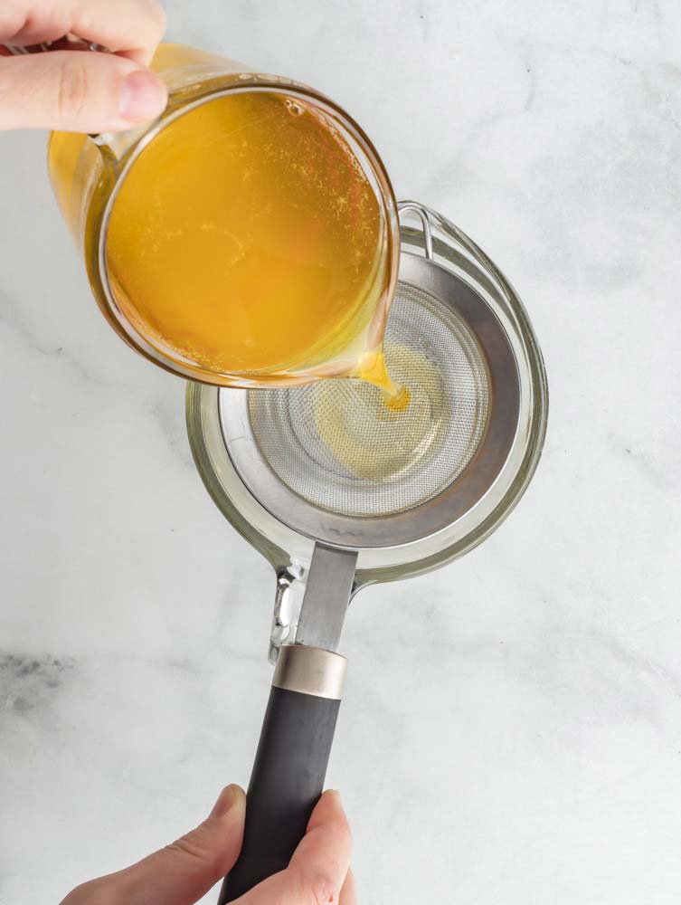 Straining ghee through a mesh strainer.