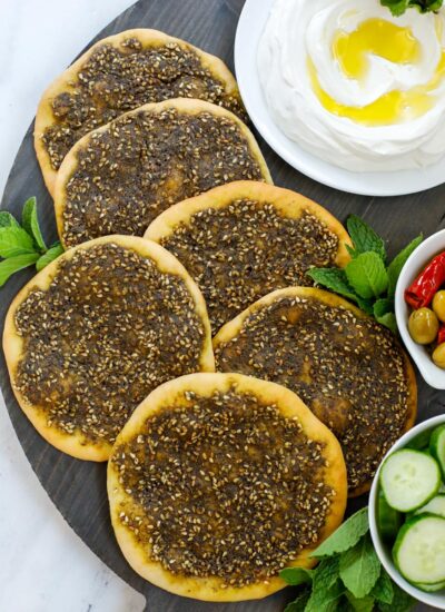 top down shot of zaatar manakeesh on a dark board with labneh, cucumber and olives