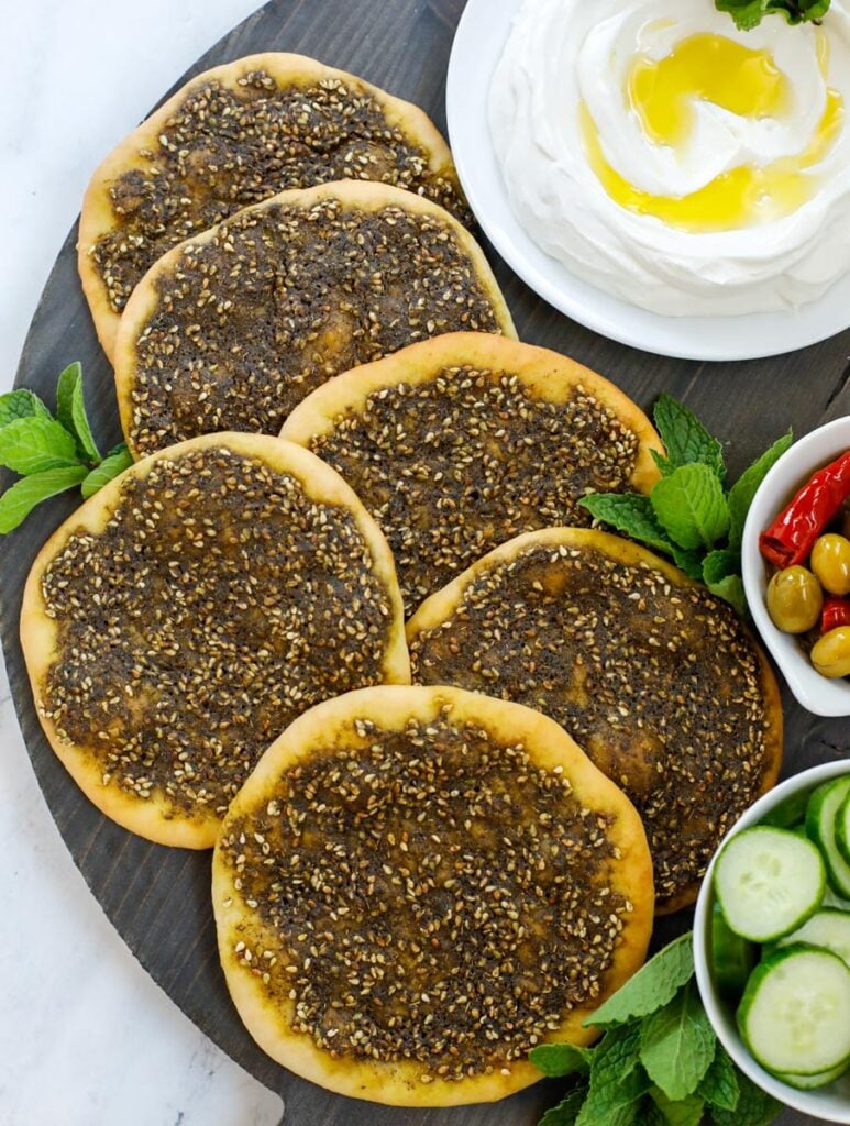 top down shot of zaatar manakeesh on a dark board with labneh, cucumber and olives