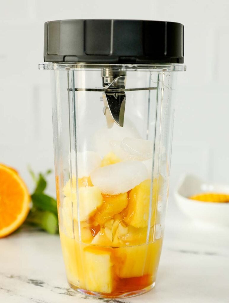 Pineapple slushie inside of a blender to be blended up.