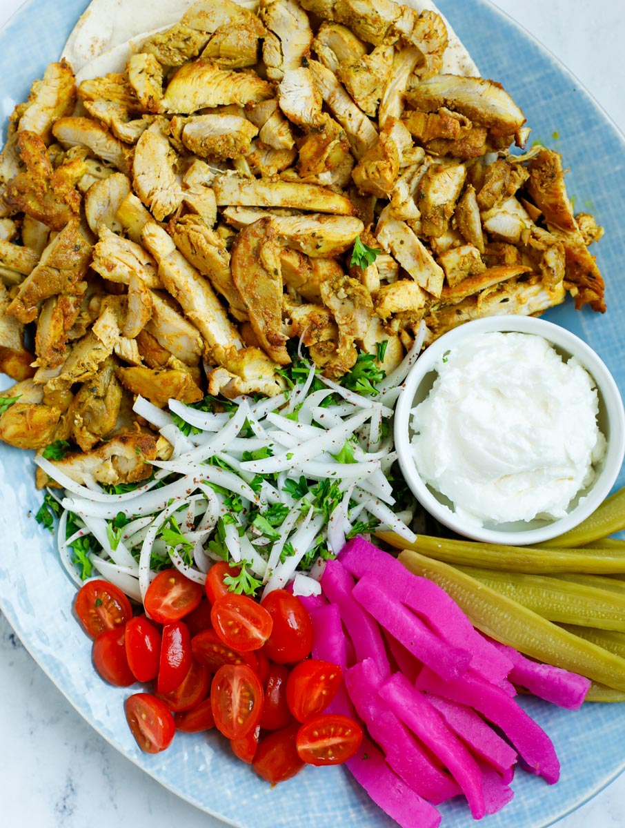 A platter of chicken shawarma with dip and sides.