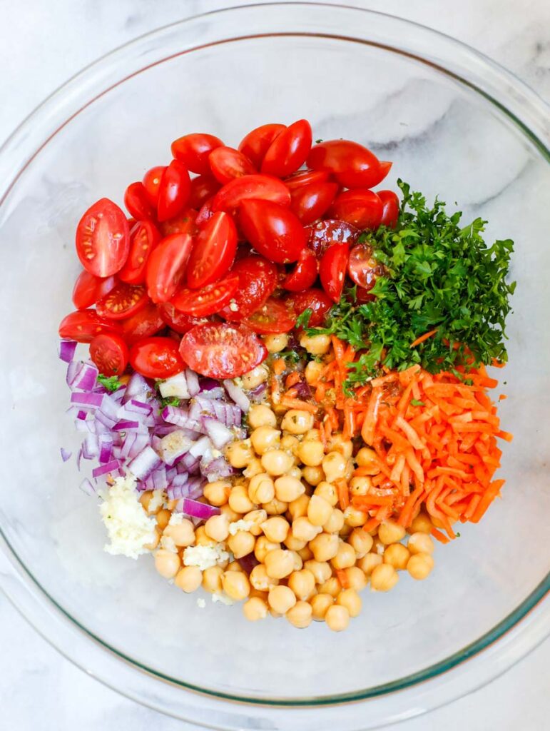 Large bowl with tomatoes, herbs, carrots, chickpeas, onions, and garlic.