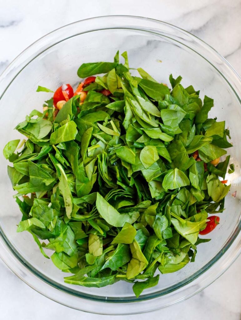 Spinach added to a bowl of salad.