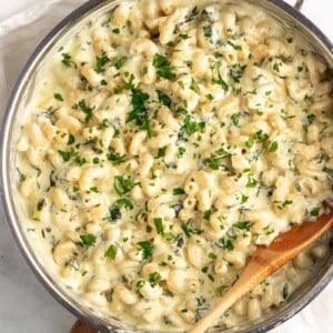 top down shot of spinach mac and cheese with wooden spoon in skillet