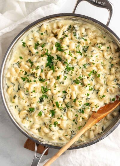 top down shot of spinach mac and cheese with wooden spoon in skillet