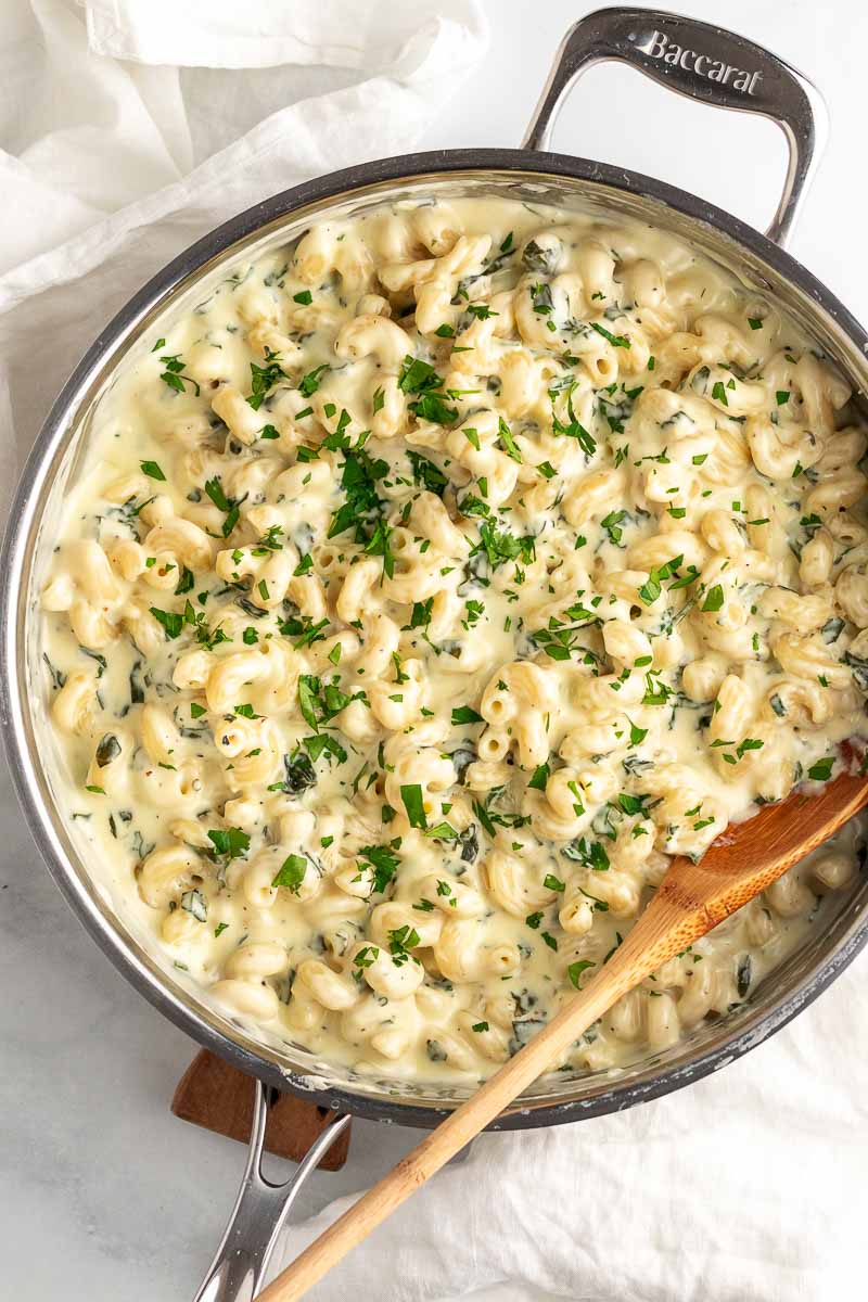 top down shot of spinach mac and cheese with wooden spoon in skillet