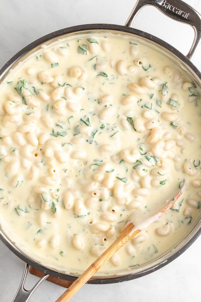 spinach mac and cheese in a skillet with a wooden spoon