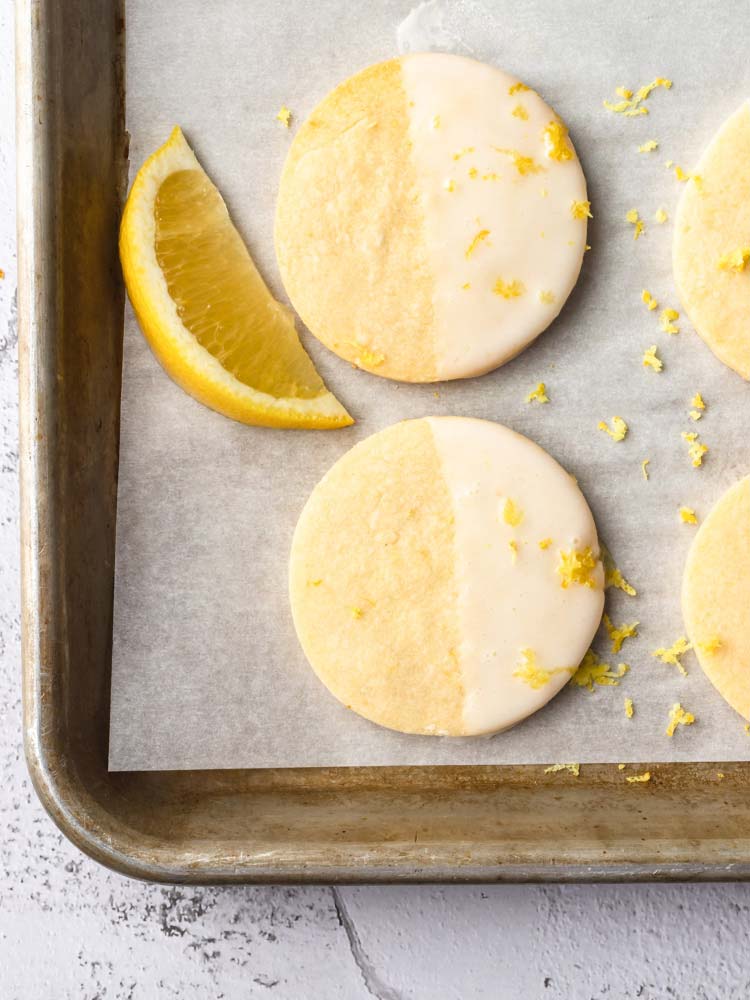 lemon cookie dipped half way into icing and places on a sheet pan. garnished with lemon zest