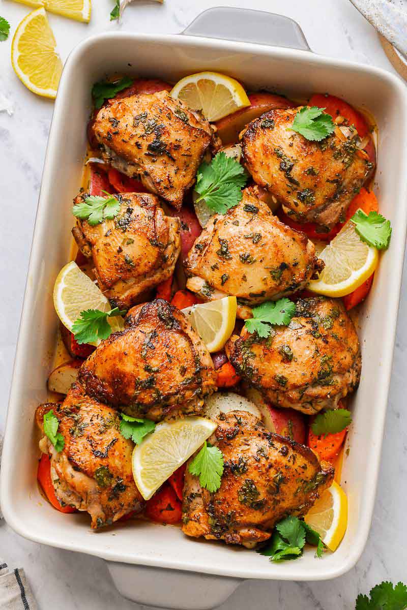 Chicken thighs in a baking dish with veggie and lemon wedges after baking