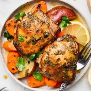 Two pieces of chicken thighs in a plate with veggies and fork