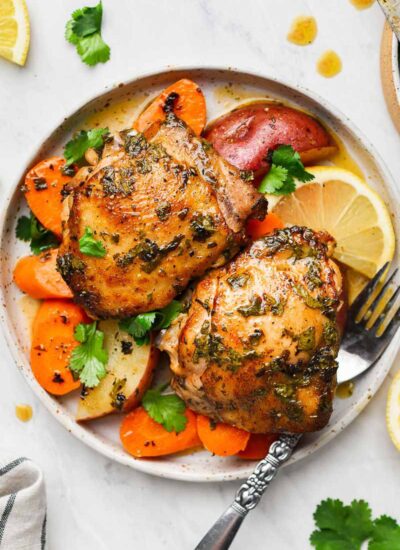 Two pieces of chicken thighs in a plate with veggies and fork