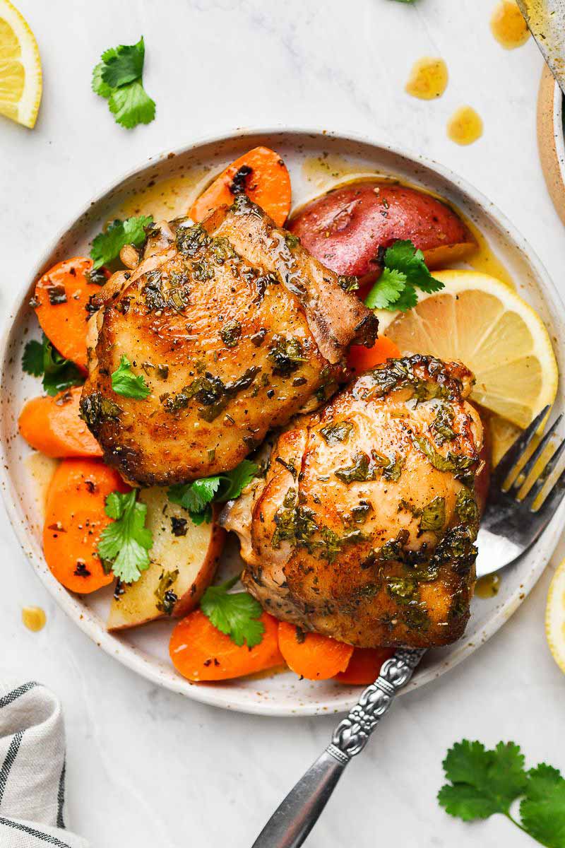 Two pieces of chicken thighs in a plate with veggies and fork